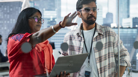 Woman and Man looking at something in front of them. Woman has computer in her hand.