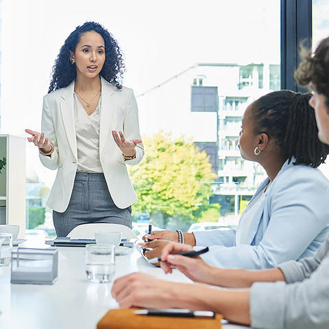Woman standing at the head of the table talking with employees sitting listening